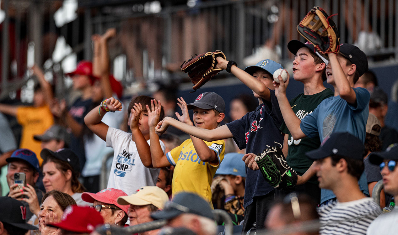 Group of excited young baseball fans reaching for a fly ball with gloves raised