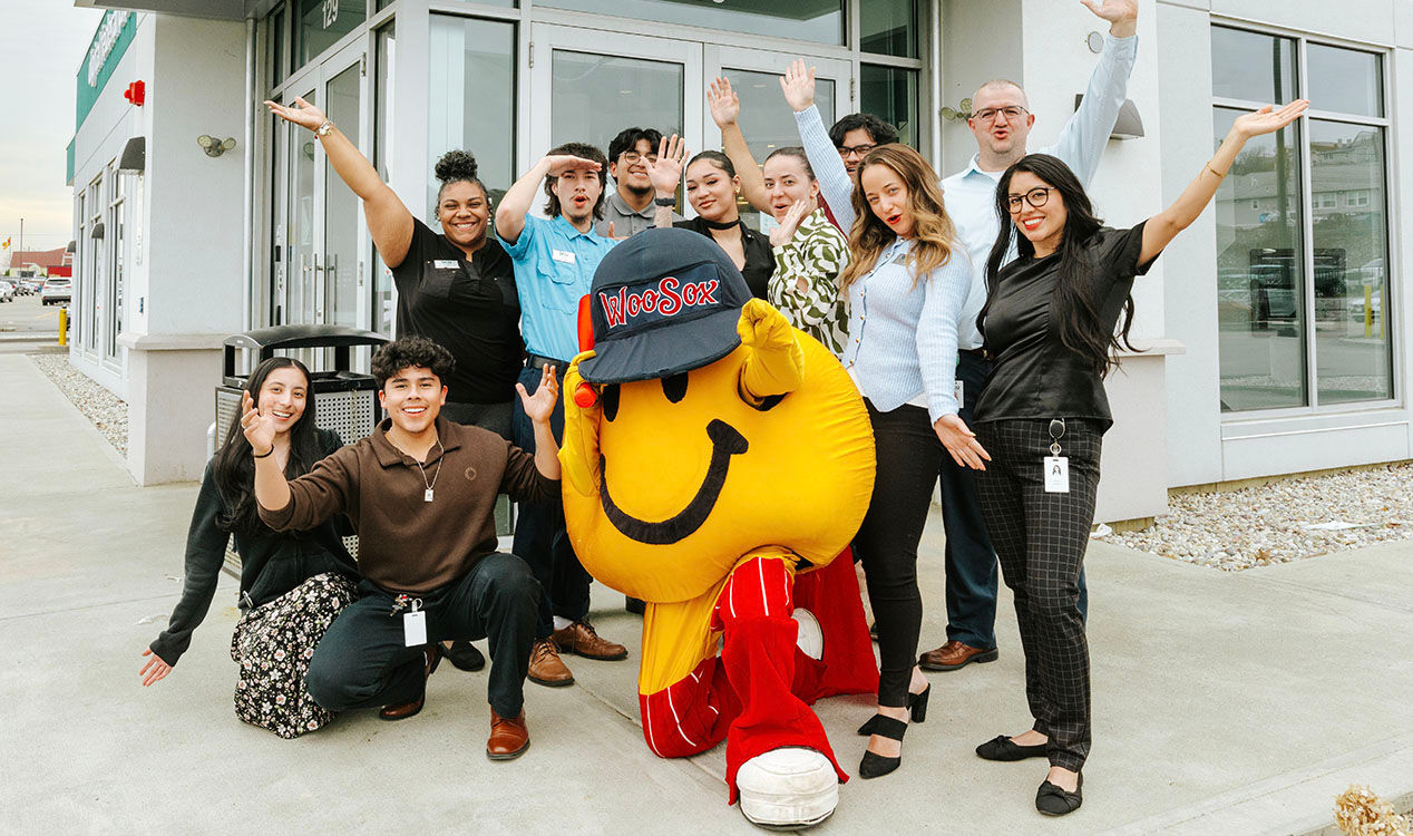 Smiley Ball, the iconic yellow mascot of the Worcester Red Sox, happily poses in front of a Worcester DCU branch entrance with DCU team members during March Member Appreciation Days.