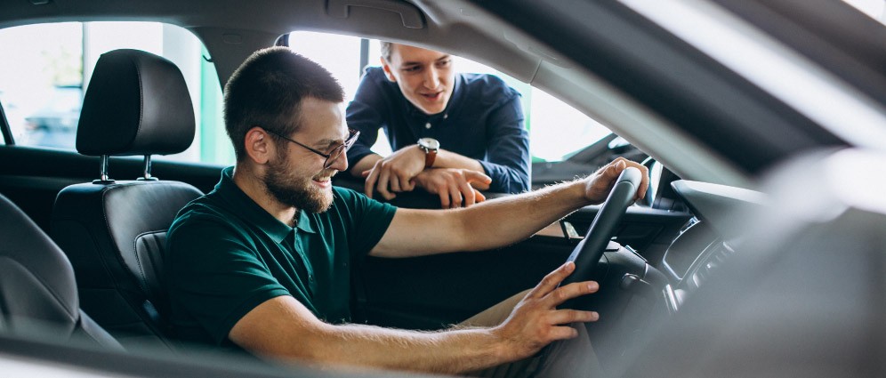 Man standing at car window selling him a car.