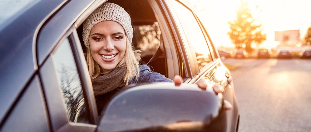 Woman gazing into the side-view mirror of her car and smiling