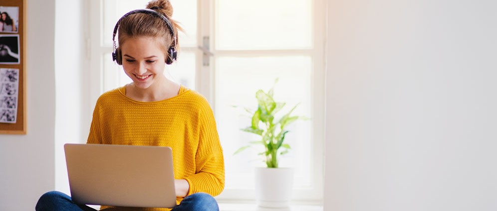 Young woman smiling listening to headphones and looking at laptop