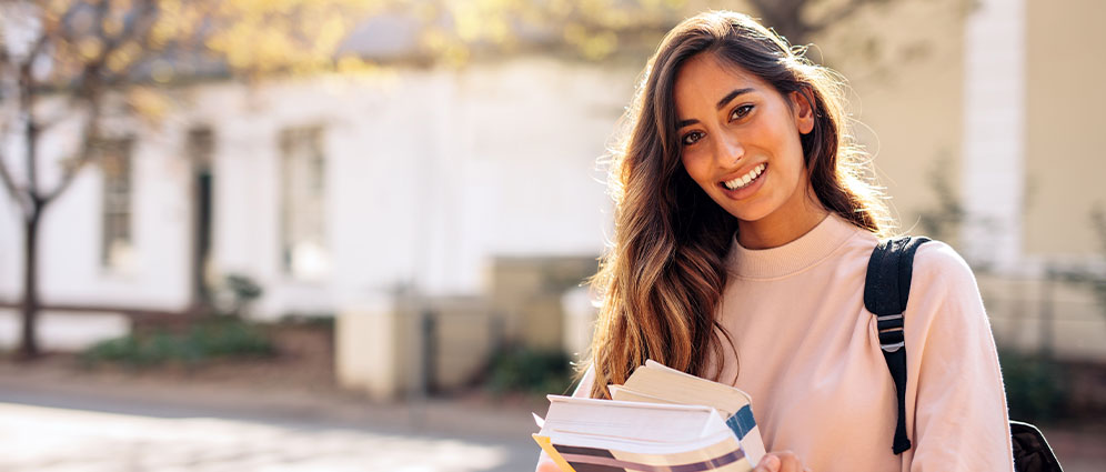 A female student smiling holding text books.