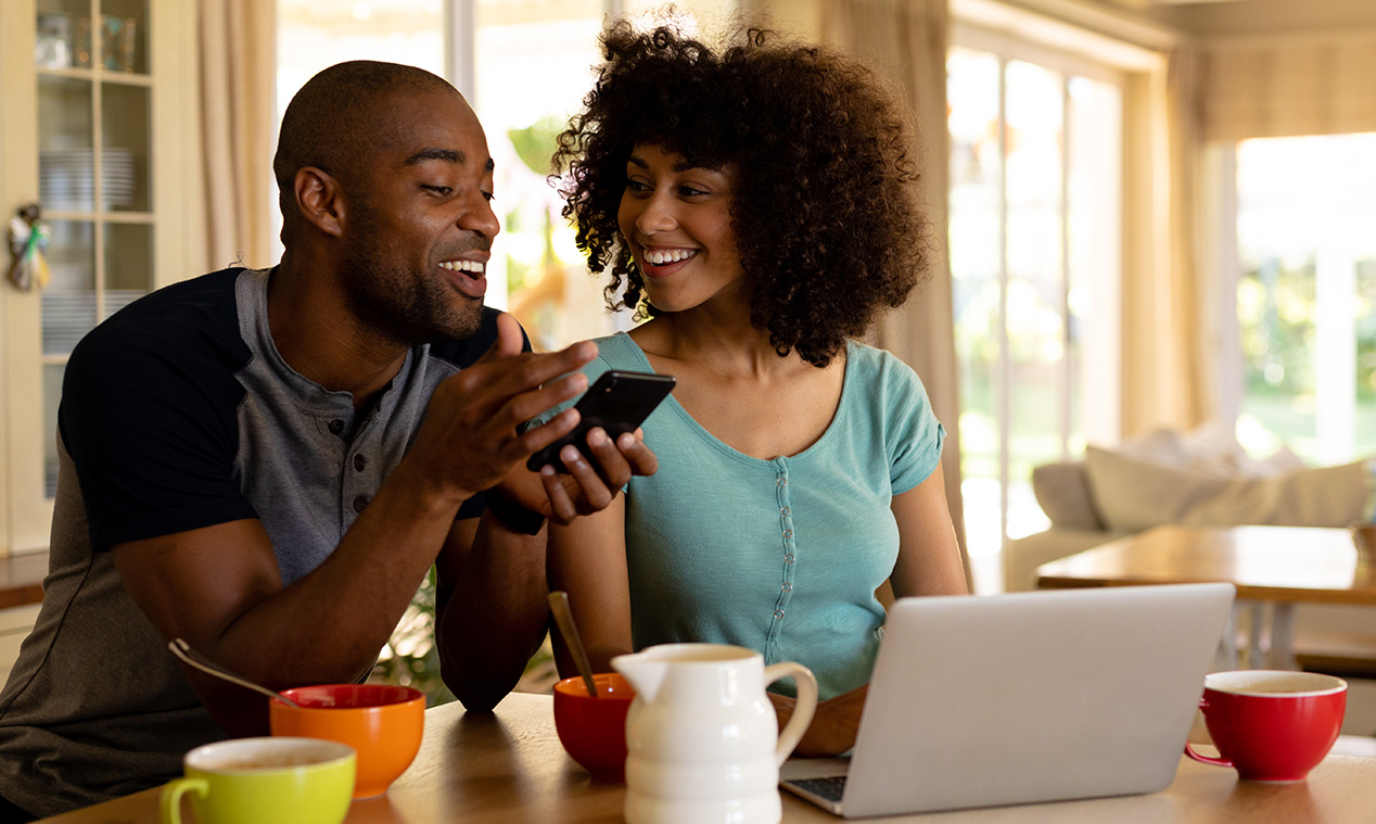 Two people using a smartphone beside a laptop
