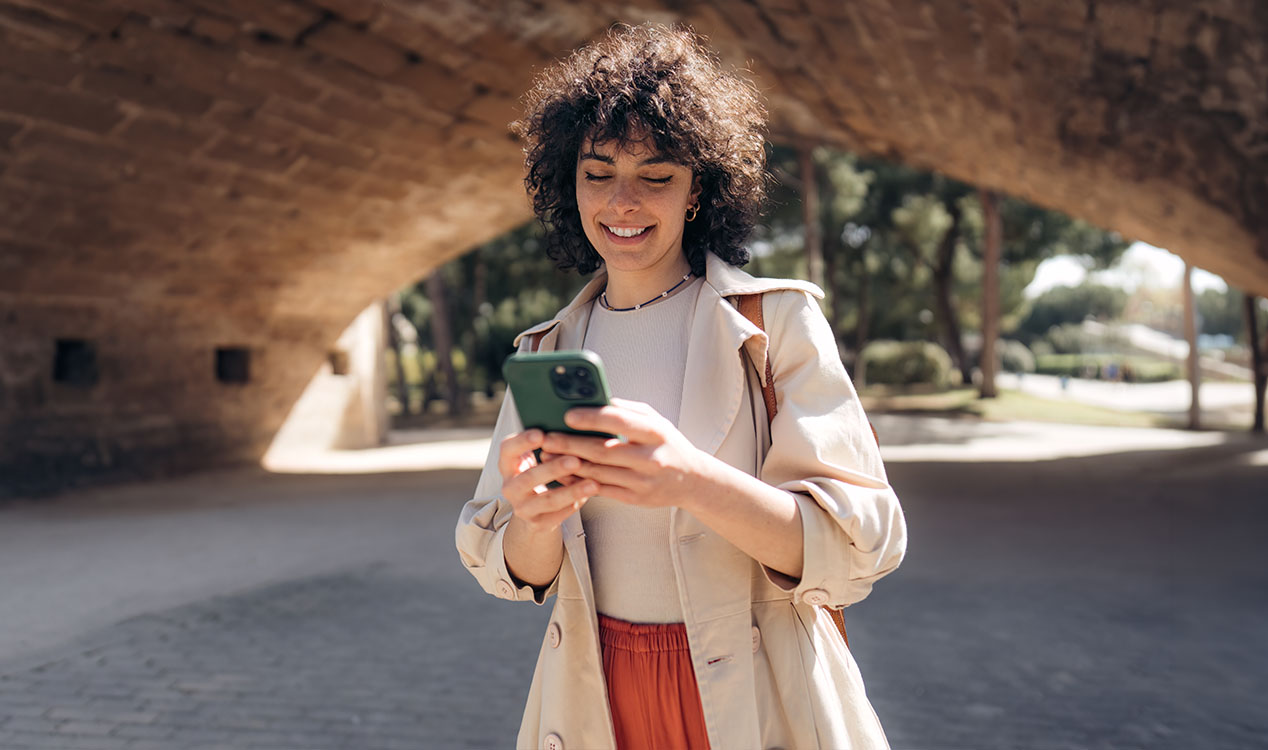 Woman smiling while holding a mobile device outside