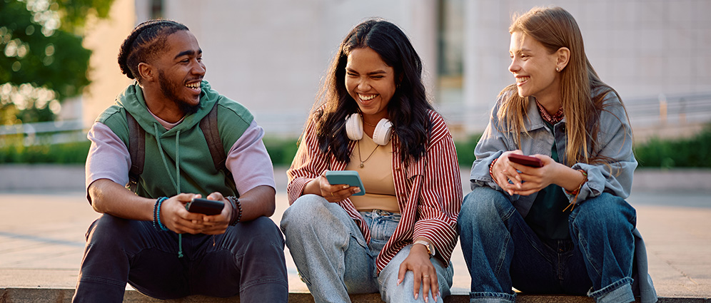 Group of Gen-Z people sitting down and smiling while holding their phones
