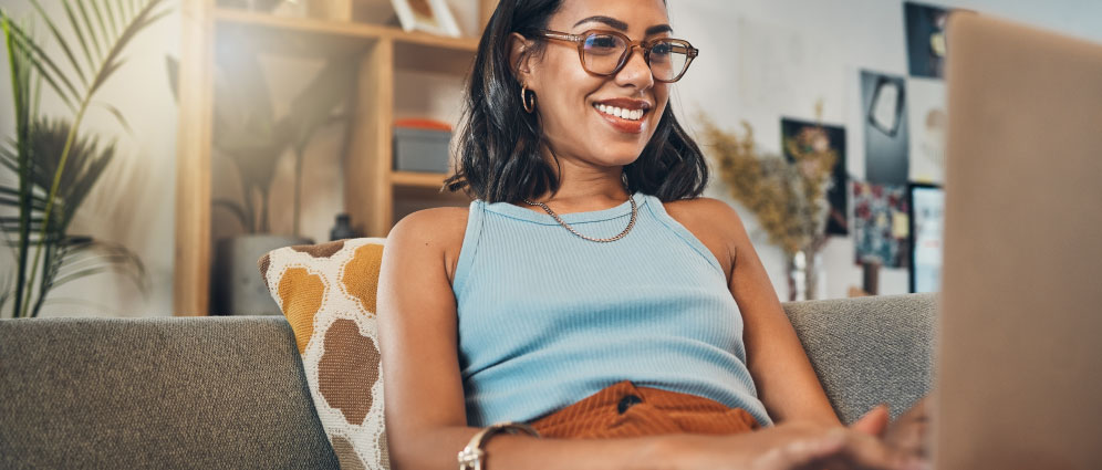 Smiling woman resting on a sofa looking at a laptop
