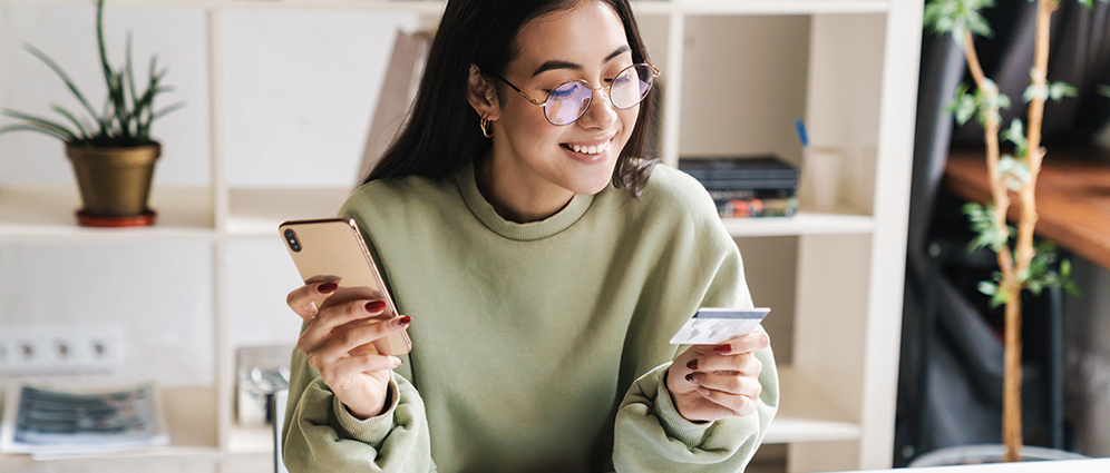 A woman holding her phone and smiling while looking at her credit card