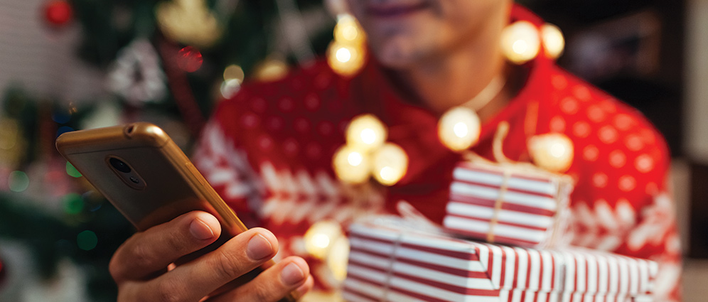 A person wearing a holiday sweater holding a mobile phone