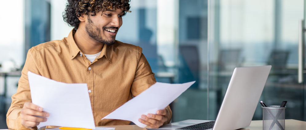 Man sitting at his laptop while holding paperwork