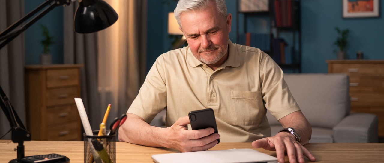 A man sitting at a desk and looking at his cell phone