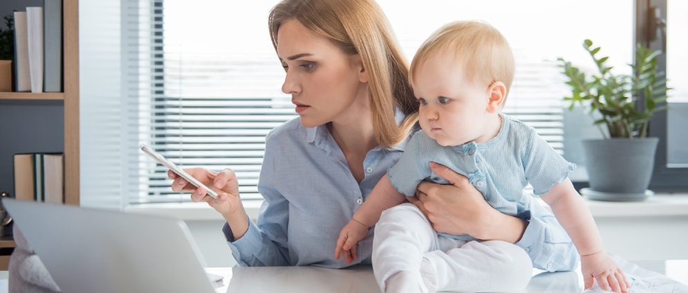 A mother looking at her phone and laptop while holding her baby