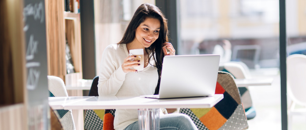 A woman smiling while sitting in a cafe with her laptop