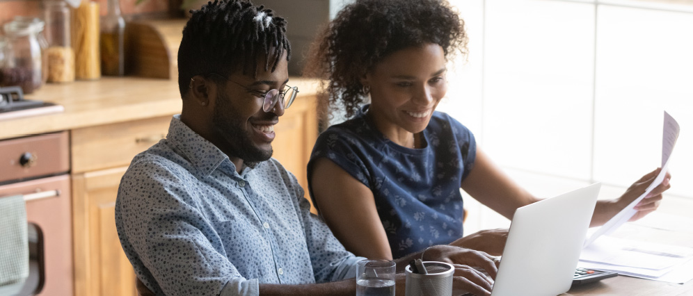 A couple smiling while looking at a laptop together