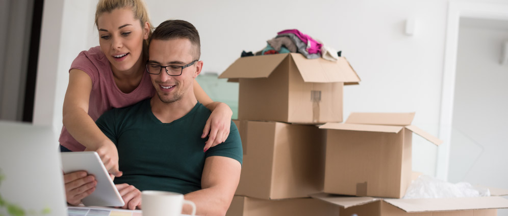 A couple smiling in front of packed moving boxes