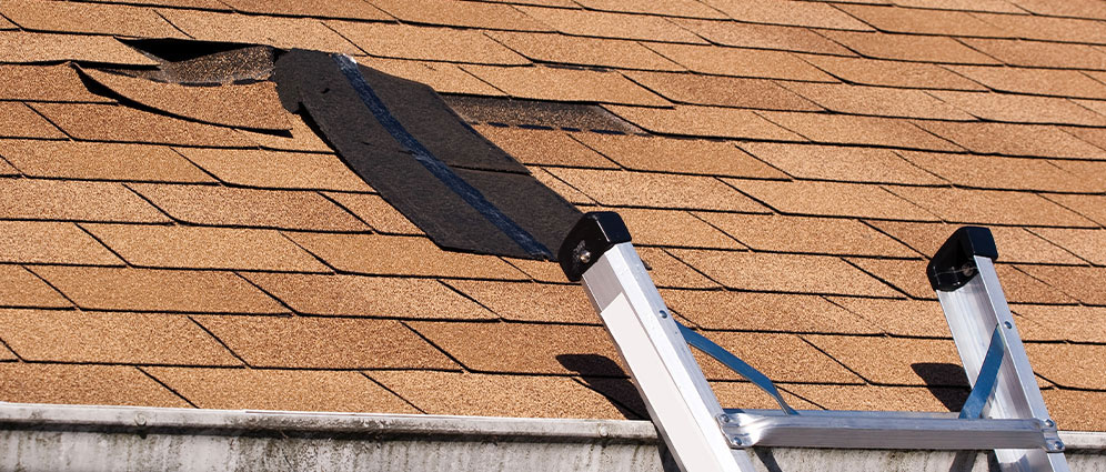 A ladder placed at the edge of a roof with loose shingles
