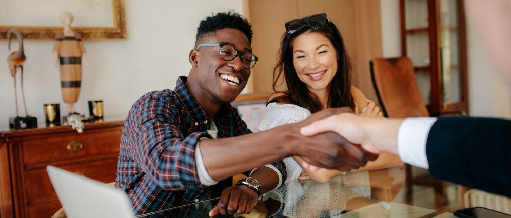 Couple smiling while shaking hands with a realtor