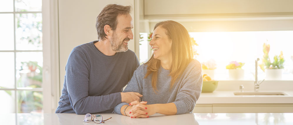 A couple sitting in their kitchen and smiling at each other