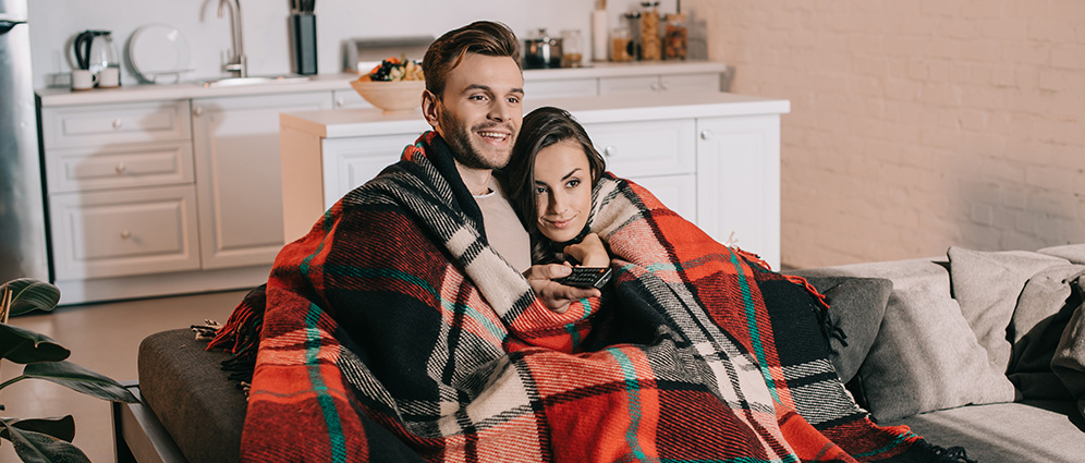 A couple cuddling under a blanket and watching TV