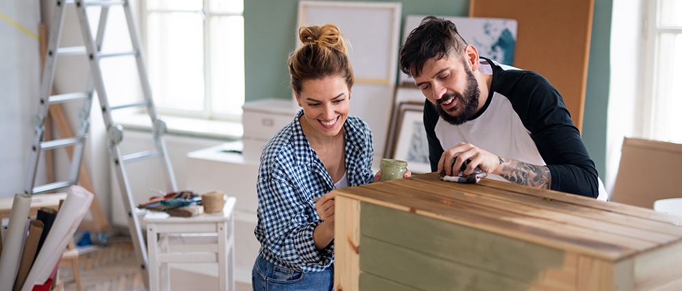 A couple smiling while staining a dresser
