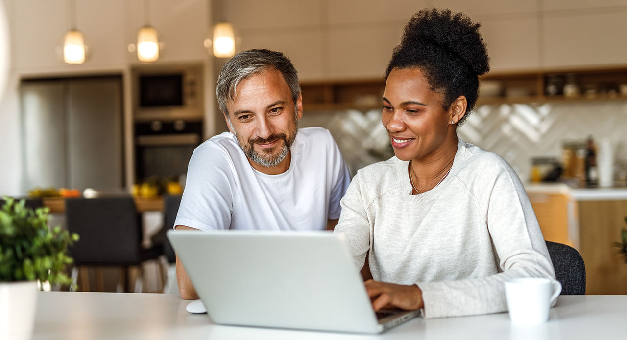 A couple smiling while typing on a laptop
